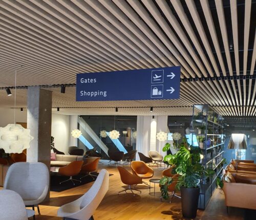 Lofthængt retningsskilt i lufthavn, der viser vej til gates og shopping