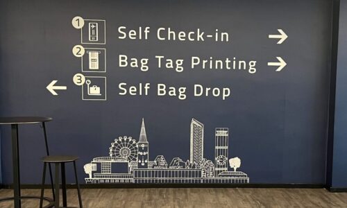 Vægdekoration i lufthavn med visuel guide til check-in i tre trin: self check-in, bag tag printing og bag drop