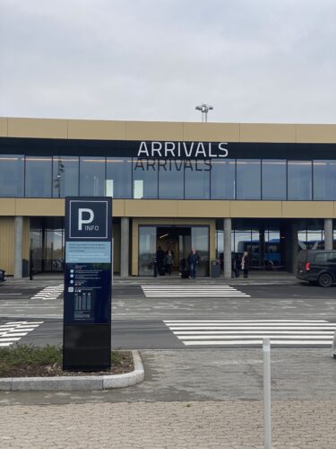 Terminalindgang til Arrivals med pylon i stål og glas i forgrunden, der viser parkeringstakster og regler